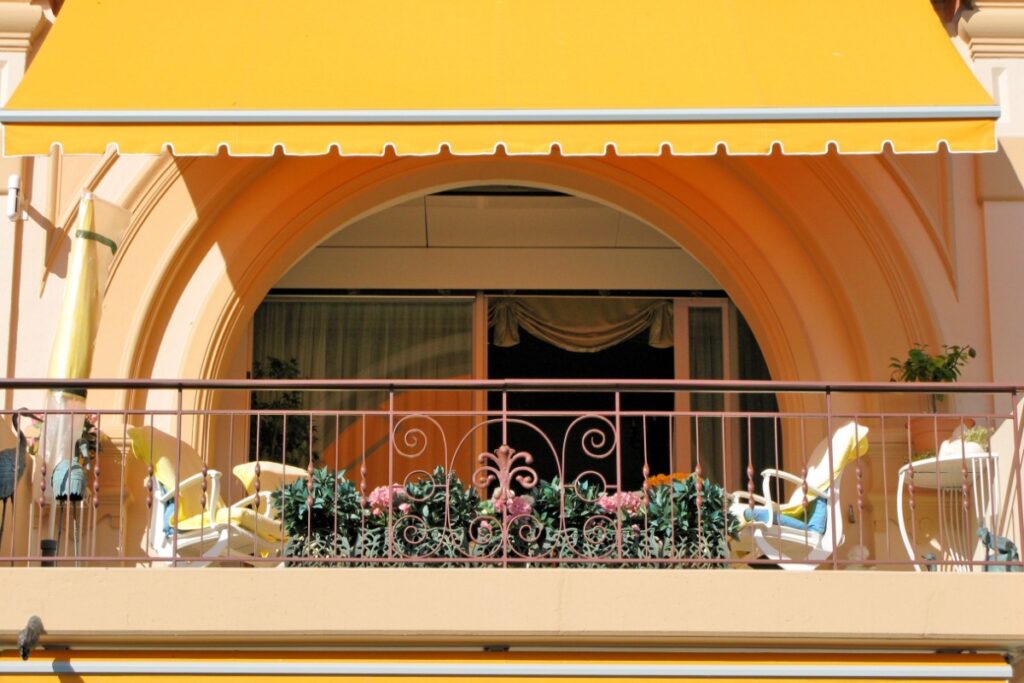 Balcone soleggiato incorniciato da un arco architettonico e ombreggiato da una vivace tenda da sole a bracci gialla
