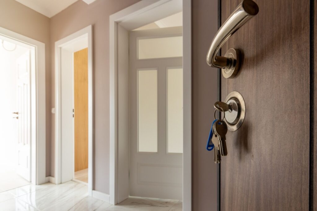 Interior hallway featuring white paneled swing doors with glass panes and brass handles opening into a sunlit room