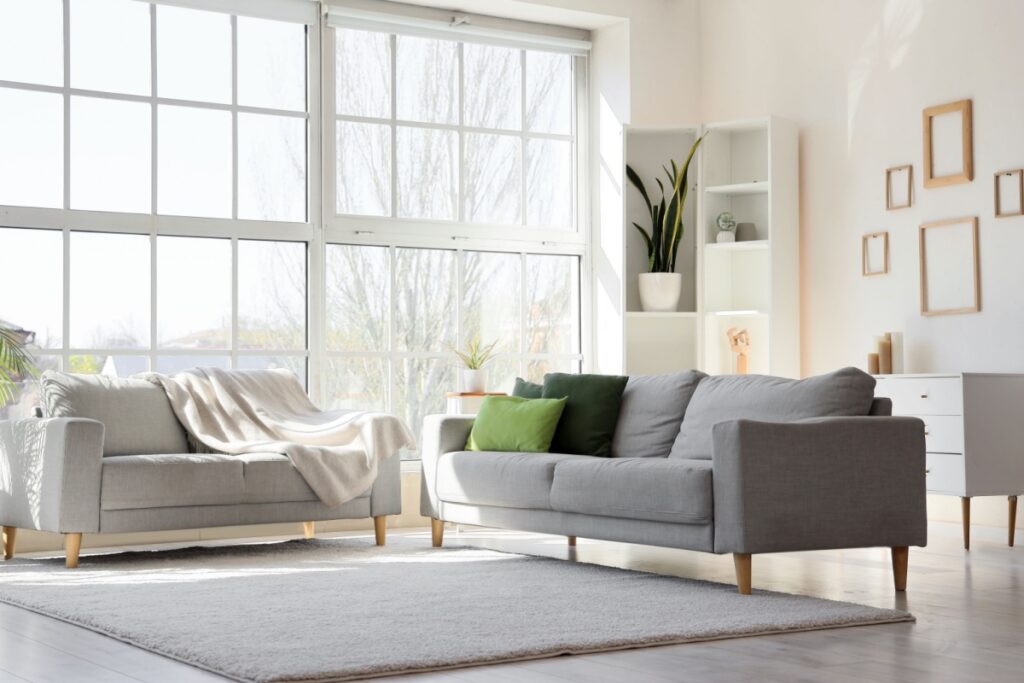 Soggiorno luminoso in stile minimalista con divani grigi dalle linee pulite, grandi finestre e arredi essenziali dai toni neutri