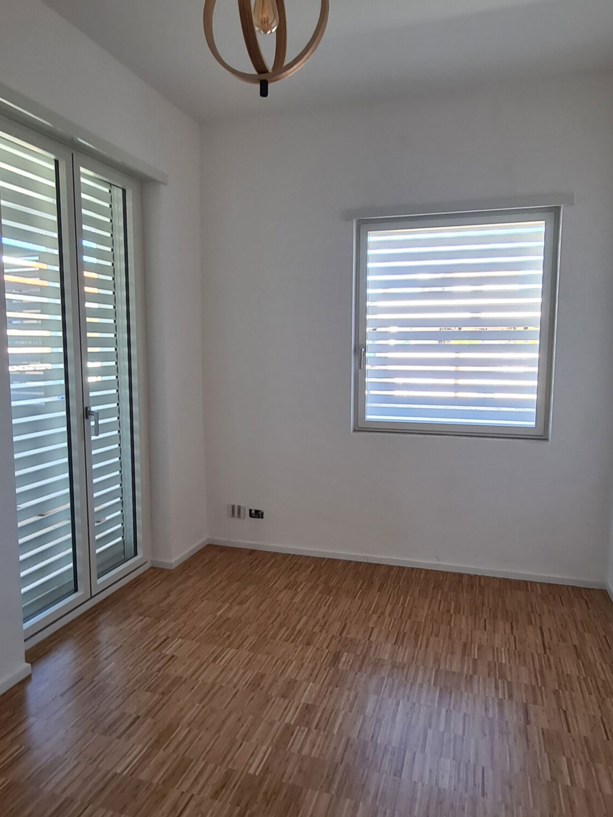Porta finestra e finestra con sistemi oscuranti integrati in una stanza con parquet
