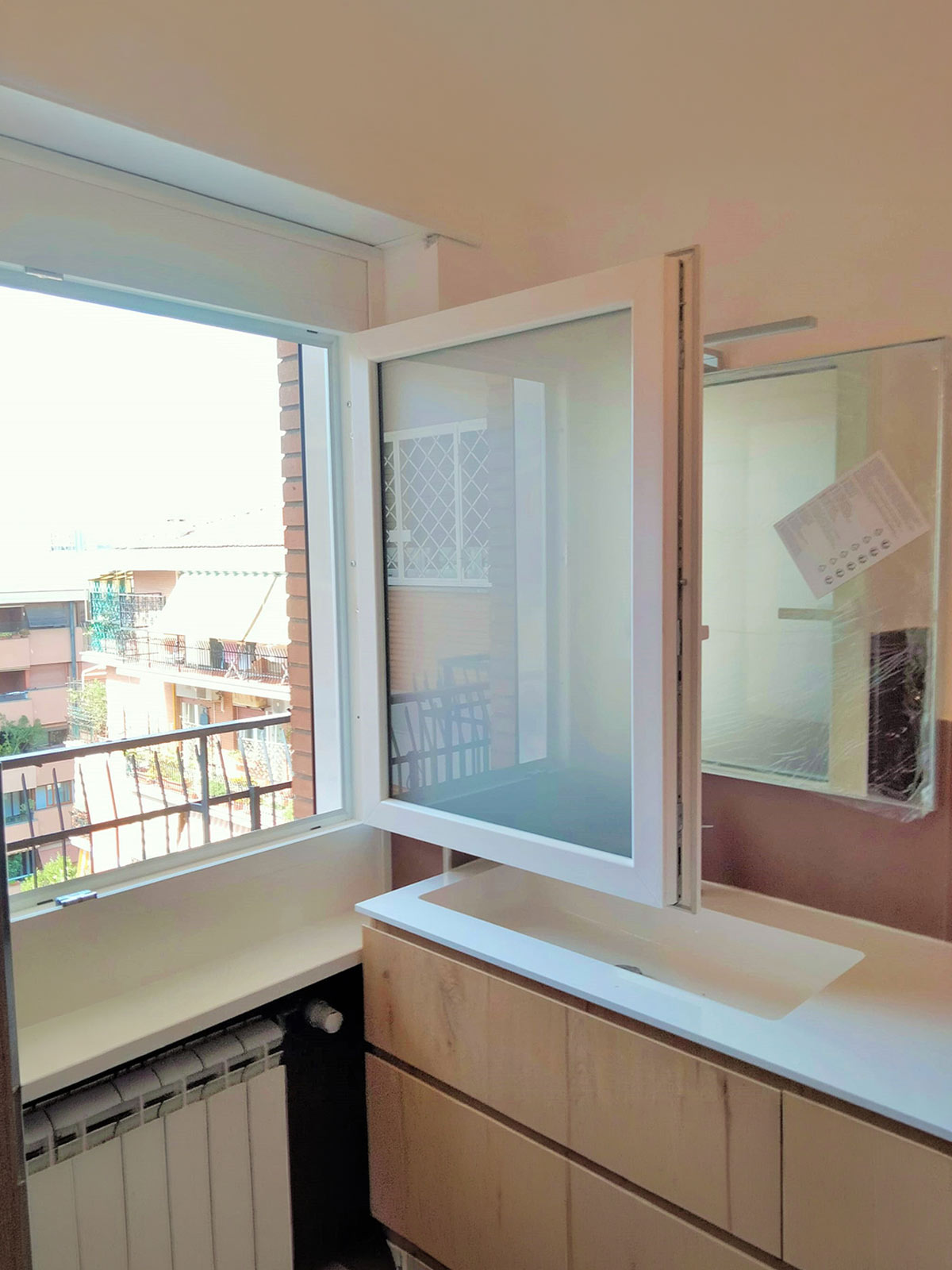 Finestra in PVC bianco aperta a battente sopra il lavabo di un bagno moderno
