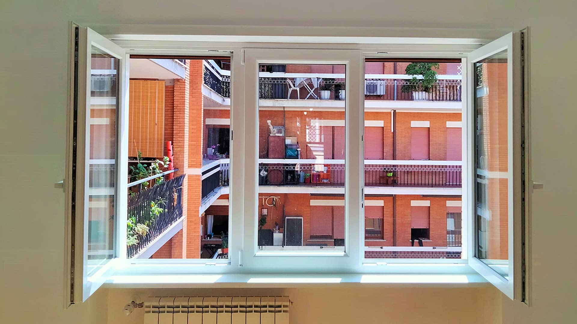 Finestra in PVC bianco a tre ante aperta su un cortile residenziale a Roma