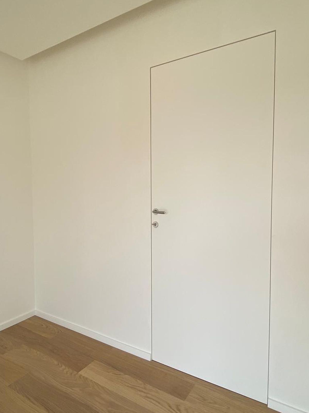 Dettaglio di una porta rasomuro bianca senza stipiti né cornici perfettamente integrata nella parete