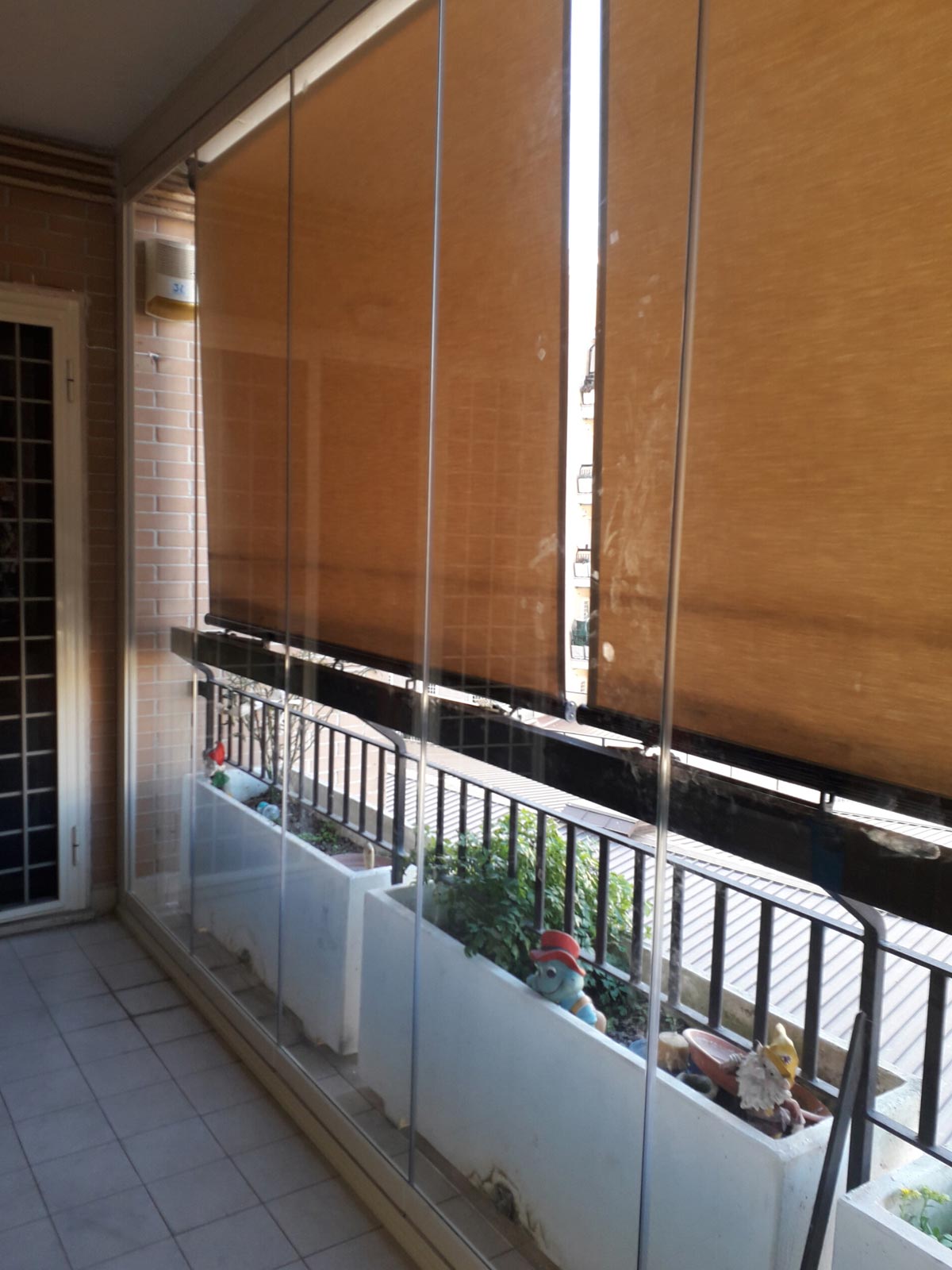 Tenda a caduta verticale in tessuto tecnico marrone installata a protezione della vetrata di un balcone