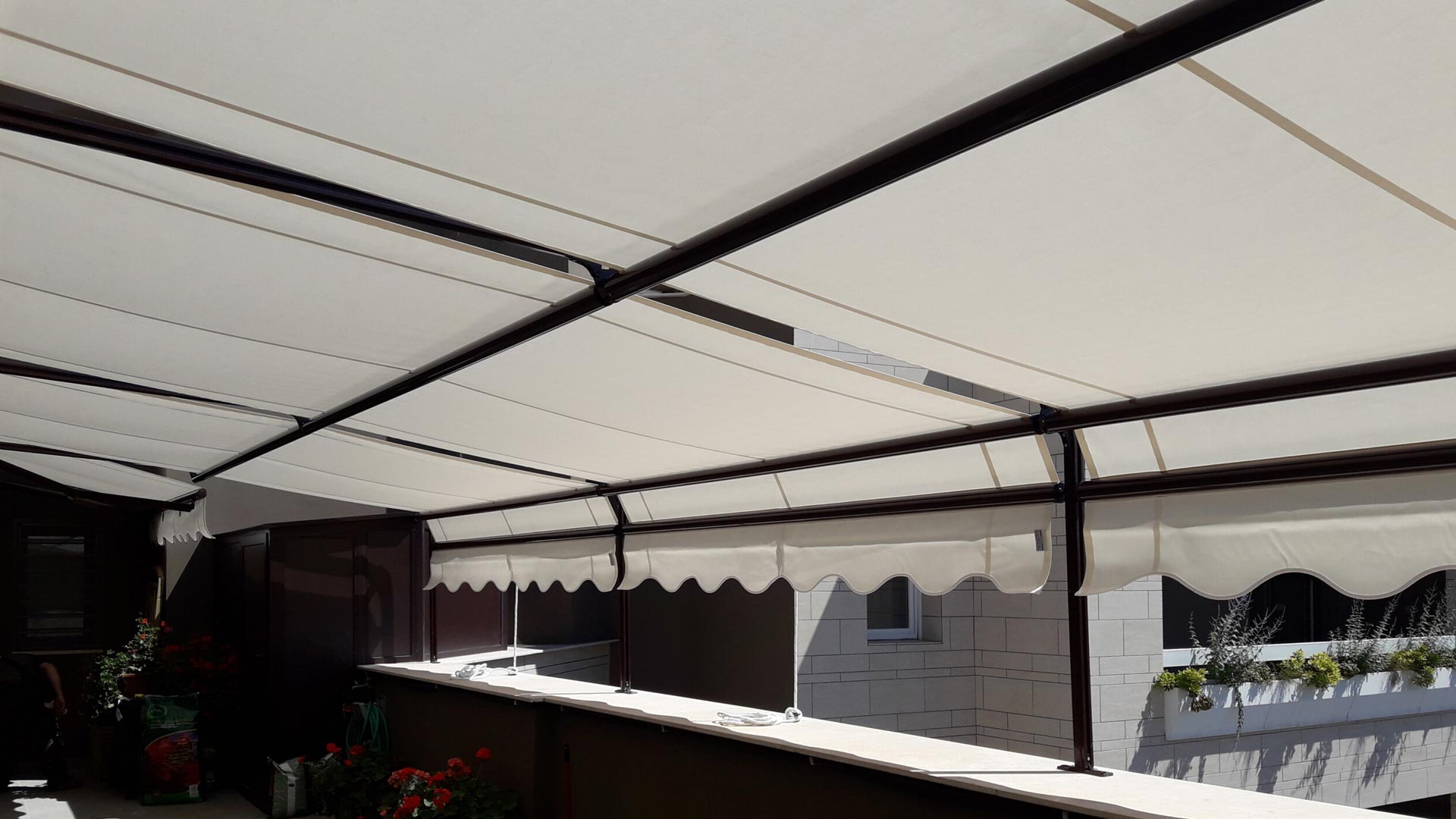 Grande tenda da sole a scorrimento con tessuto chiaro e struttura in alluminio marrone su un terrazzo