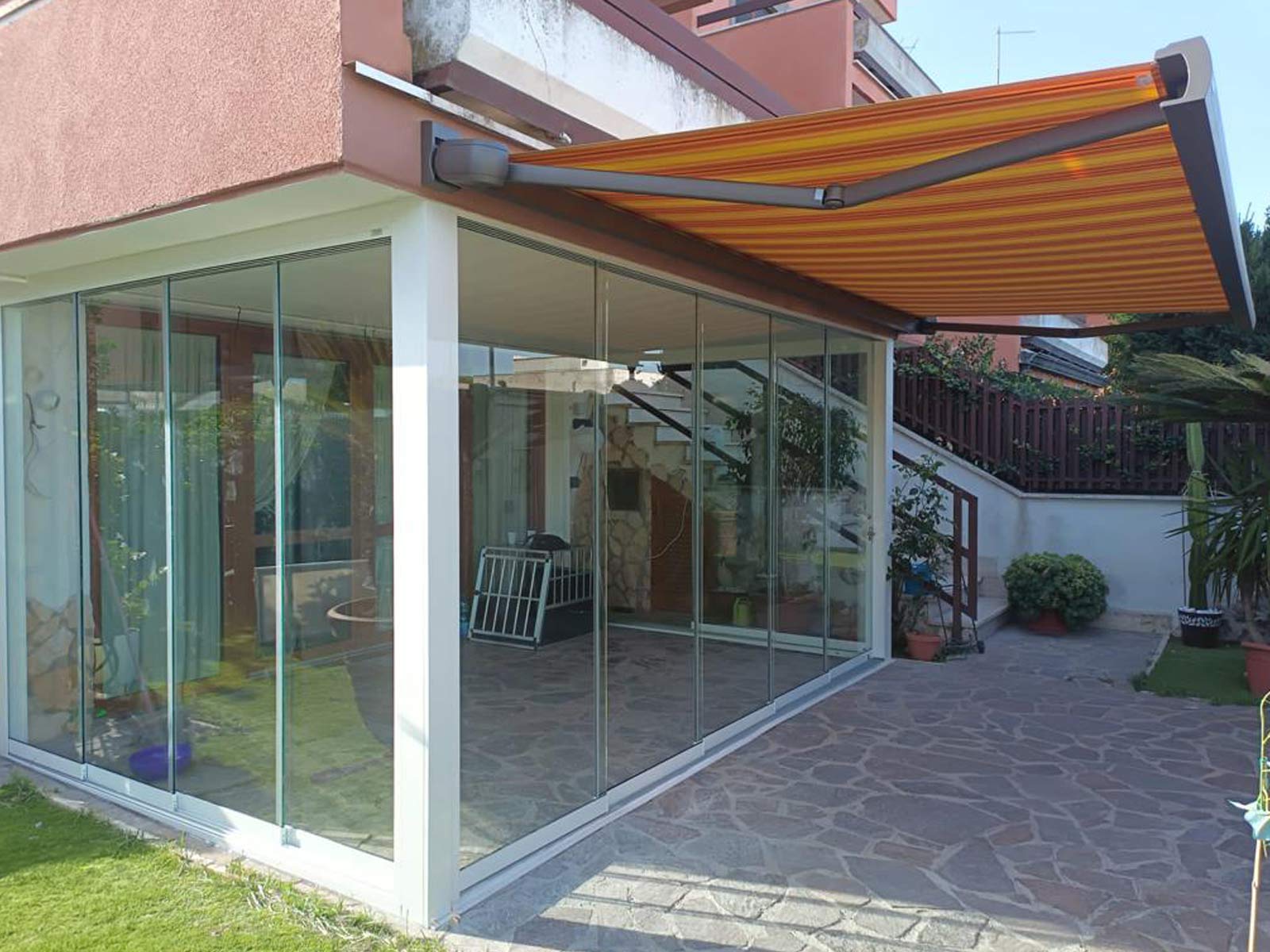 Portico esterno chiuso con vetrate panoramiche scorrevoli e tenda da sole a strisce