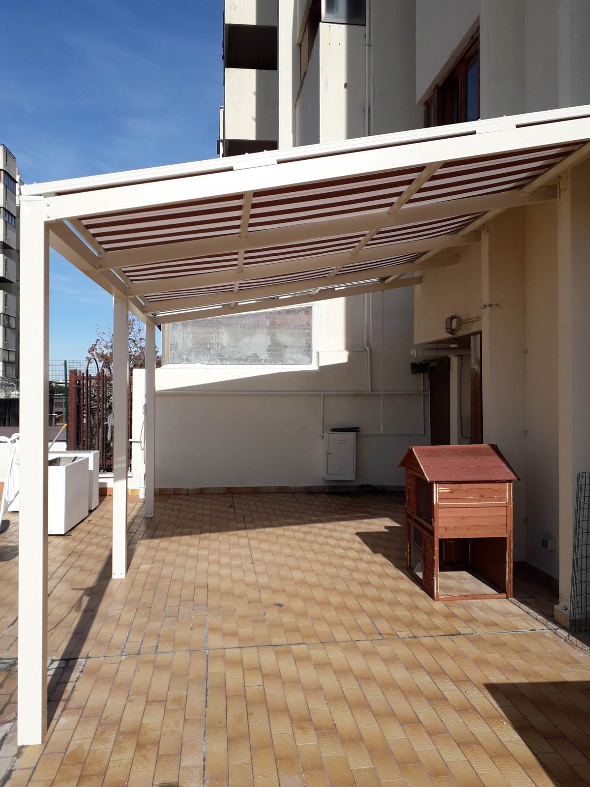 Pergotenda addossata a parete con telo a strisce per la copertura e l'ombreggiatura di un terrazzo